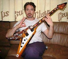 a man sitting on a couch holding an electric guitar in front of him with his right hand