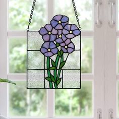 a stained glass window with purple flowers hanging from it's side, next to a potted plant