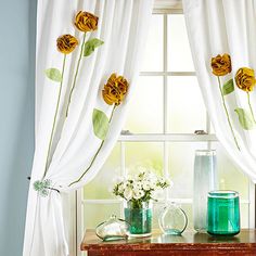 a window with white curtains and flowers in vases on the table next to it