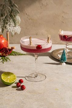 two glasses filled with drinks sitting on top of a table next to limes and cranberries