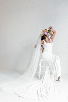 A Bride Holding A Bridal Bouquet Sitting On A White Stool With A White Background.