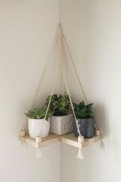 three potted plants are hanging from a shelf in the corner of a white room