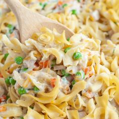 a wooden spoon full of chicken noodle casserole with peas and carrots