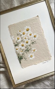 a painting with white and yellow daisies in a gold frame on a tablecloth