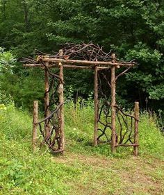 a wooden structure made out of branches in the grass and trees behind it are bushes