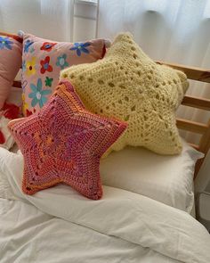 three crocheted stars sit on top of a bed with white sheets and pillows