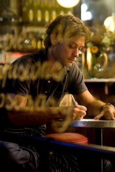 a man sitting at a bar writing on his cell phone while looking through the window