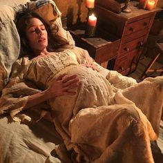 a pregnant woman laying in bed with candles