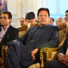 two men sitting on chairs in front of other men and one is looking at the camera