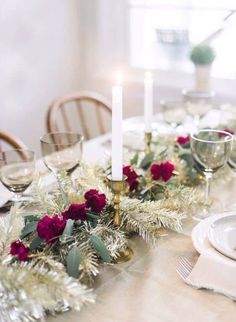 the table is set with candles, plates and glasses for christmas dinner guests to enjoy