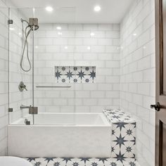 a white tiled bathroom with blue and gray stars on the bathtub, shower head, and toilet seat