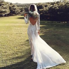 the back of a woman in a white wedding dress walking across a lush green field