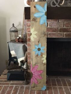 a wooden sign with flowers painted on it sitting in front of a brick fire place