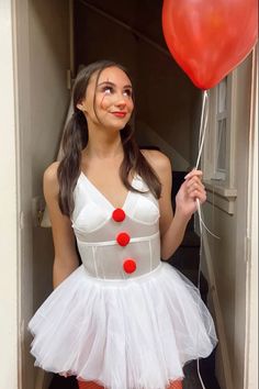 a woman in a white dress holding a red balloon and posing for the camera with her face painted on