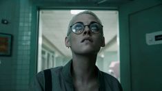 a woman with glasses looking up into the sky in a hallway at an office building