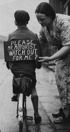 an old black and white photo of a woman teaching a boy how to ride a bike