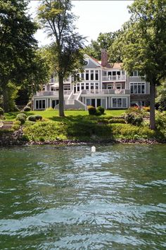 a large white house sitting on top of a lush green hillside next to a lake