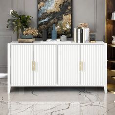 a white cabinet with books and vases sitting on it's sideboard next to a painting