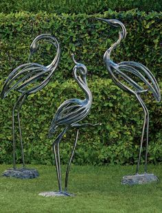 two metal flamingos standing next to each other on top of a grass covered field