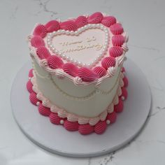 a heart - shaped cake with pink icing and white frosting is on a plate