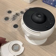 a person holding a camera next to some plastic containers and an object on a table