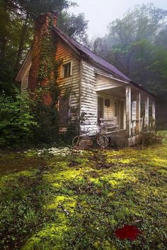 an old run down house in the middle of a field with green grass and trees