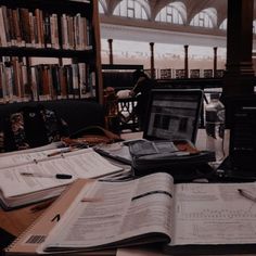 an open laptop computer sitting on top of a wooden desk next to books and papers