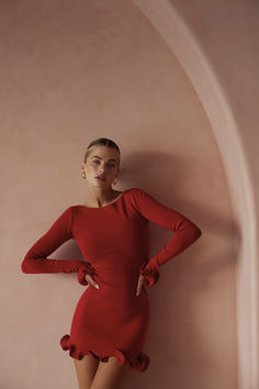 a woman in a red dress leaning against a wall with her hands on her hips