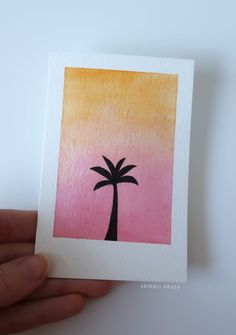 a hand holding up a small card with a palm tree painted on the front and bottom