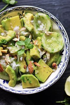 a bowl filled with sliced avocado, nuts and cilantro on top of a wooden table