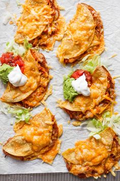 tortillas with cheese, lettuce and tomato on top sitting on a piece of parchment paper