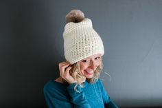 a woman wearing a white knitted hat with a pom - pom