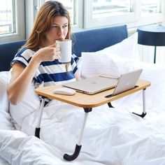 a woman sitting in bed holding a coffee cup and laptop