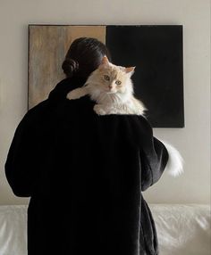 a woman holding a cat in her arms while standing next to a painting on the wall