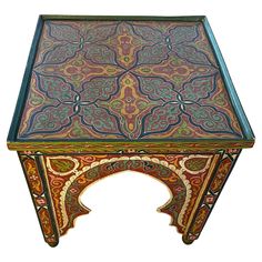 an intricately designed table with blue and red paint on the top, sitting against a white background