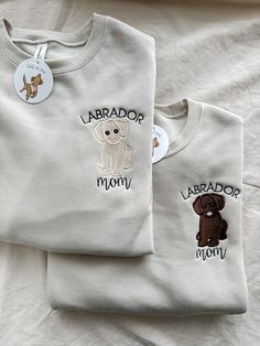 two shirts with embroidered dogs on them sitting on top of a white bed sheet, next to each other