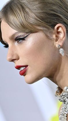 a close up of a woman with red lipstick and silver jewelry on her face, looking off to the side