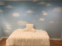 a white bed sitting in a bedroom next to a wall with clouds painted on it