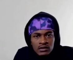 a man in a black hoodie and purple bandana looks at the camera with an intense look on his face