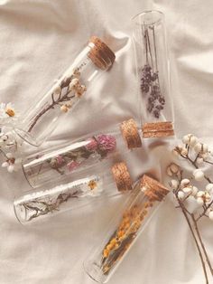 four glass bottles with dried flowers in them on a white cloth covered tablecloth,