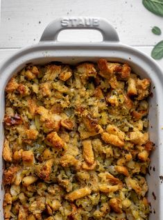 a casserole dish filled with stuffing and vegetables on top of a white table