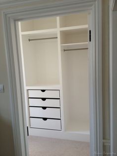 an empty closet with white drawers and black handles