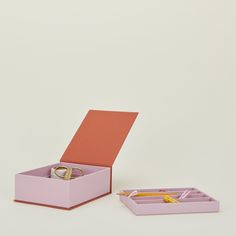 an open pink box with two gold rings in it next to a pen and pencil holder