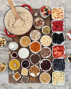 a wooden table topped with bowls filled with cereals and fruit next to other foods