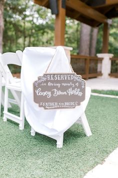 two white chairs sitting on top of a grass covered field next to a wooden sign