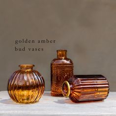 three glass vases sitting next to each other on a white surface with the words golden amber bud vases