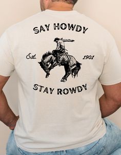 Bring a piece of the rodeo to your wardrobe with this Say Howdy Stay Rowdy bronc riding tee. The design features a western-style cowboy riding a bronc graphic. The perfect choice for any rodeo enthusiast. This shirt is crafted from 100% jersey knit cotton, delivering a great balance of style, durability, and comfort, making it ideal for everyday wear. *CARE INSTRUCTIONS Shirts should be washed in cold water, inside out and dried on low heat or hung to dry. Avoid ironing over printed area. * All Cowboy Apparel Men, Cowboy T Shirt Designs, Graphic Print Crew Neck T-shirt For Country Events, Western-themed Crew Neck T-shirt, Rodeo Design, Horse Sayings, Howdy Shirt, Cowboy Graphic, Bronc Riding