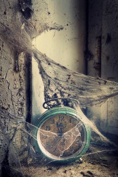 an old green clock sitting on the side of a building next to a spider web