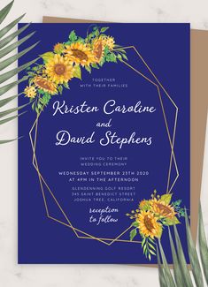 a blue wedding card with sunflowers and greenery in the middle, on top of a marble table