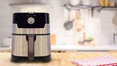 a stainless steel air fryer sitting on top of a wooden table next to a red and white checkered cloth